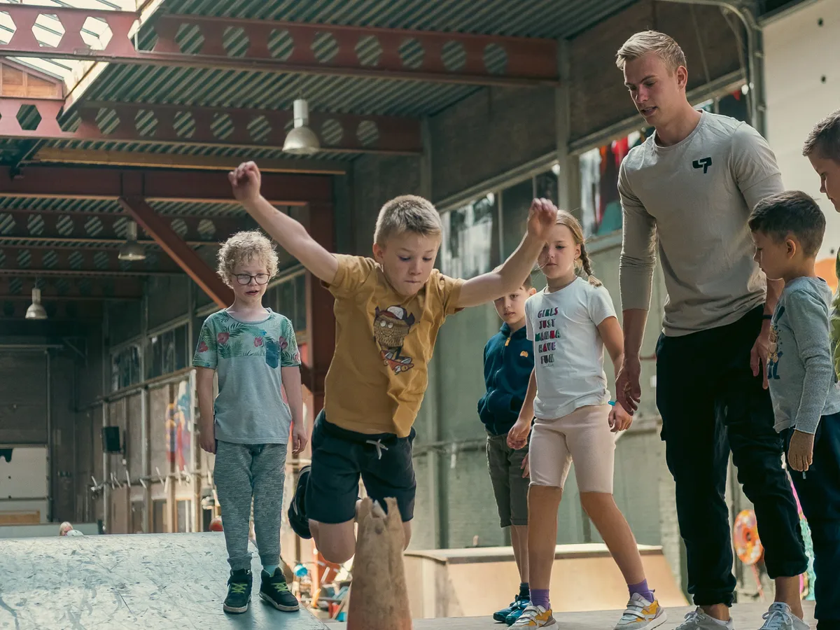 Leerling springt over een pion tijdens een freerun-clinic terwijl de groep en de coach toekijken