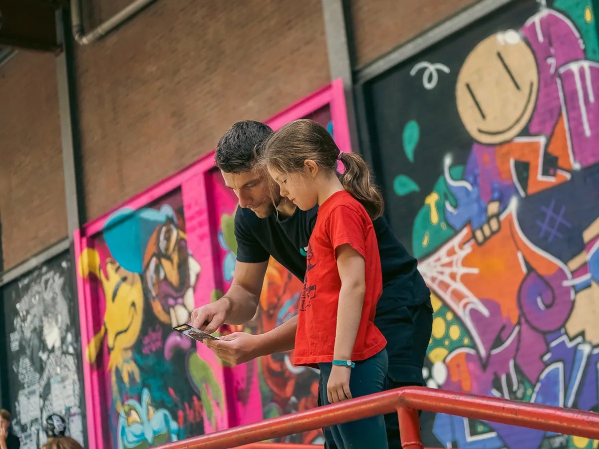 Coach bekijkt samen met een leerling een challenge-kaart tijdens een freerunles